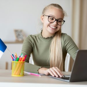 Cheerful girl with flag of France using laptop